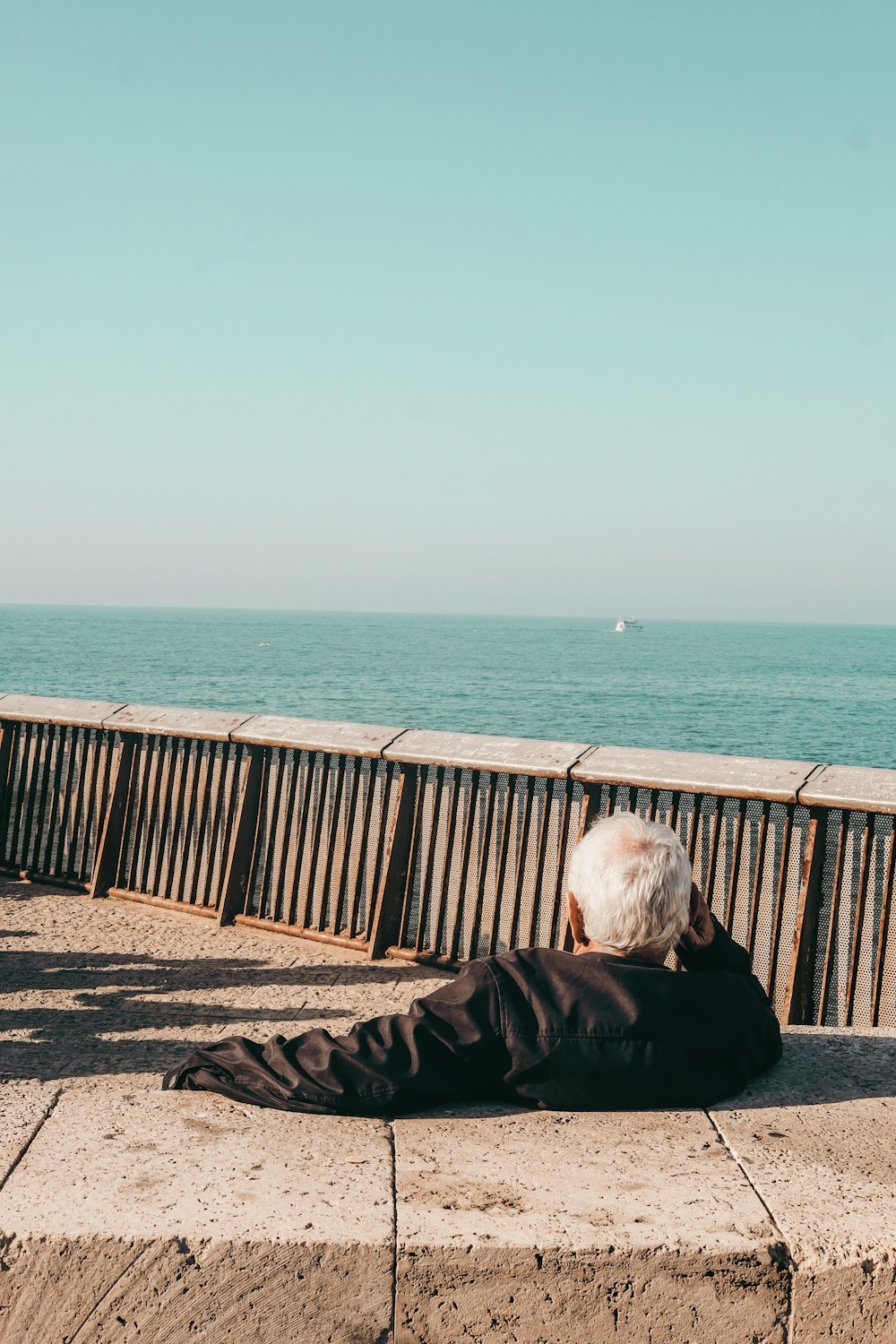 Persona in giacca nera che si siede sulla panchina di legno marrone vicino al mare durante il giorno