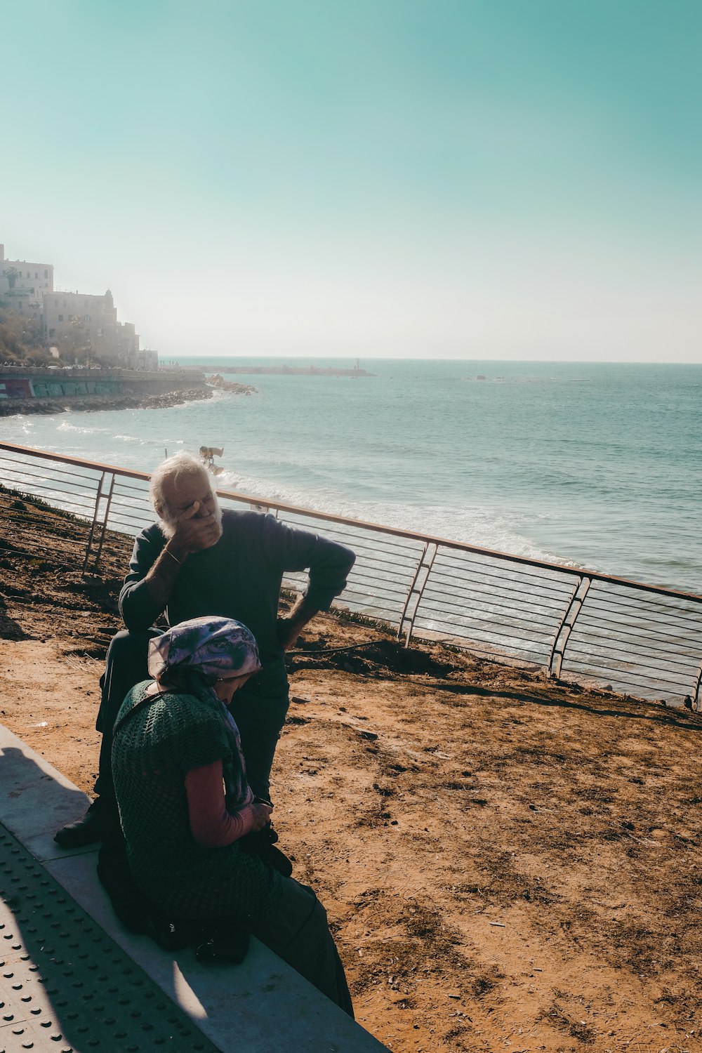 Femme en veste noire assise sur le sable brun près du plan d’eau pendant la journée