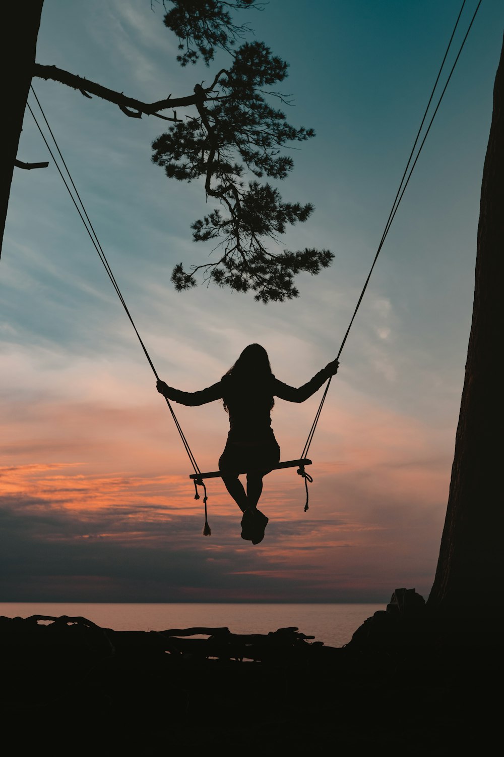 silhouette of person sitting on swing during sunset