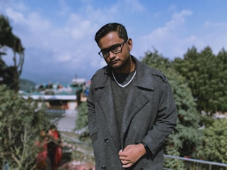 man in gray coat standing near green trees during daytime