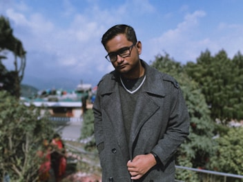 man in gray coat standing near green trees during daytime