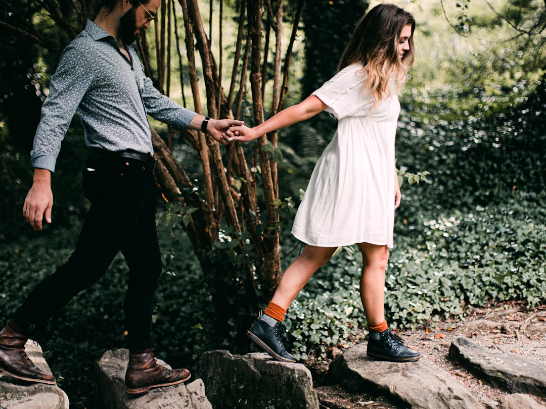 man and woman holding hands while walking on forest during daytime