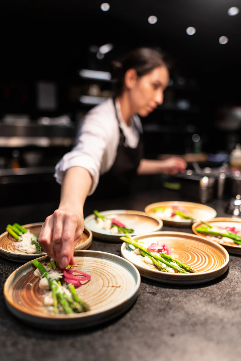 Chef's hand reaches for a plate with a selection of roasted vegetables and grilled meats