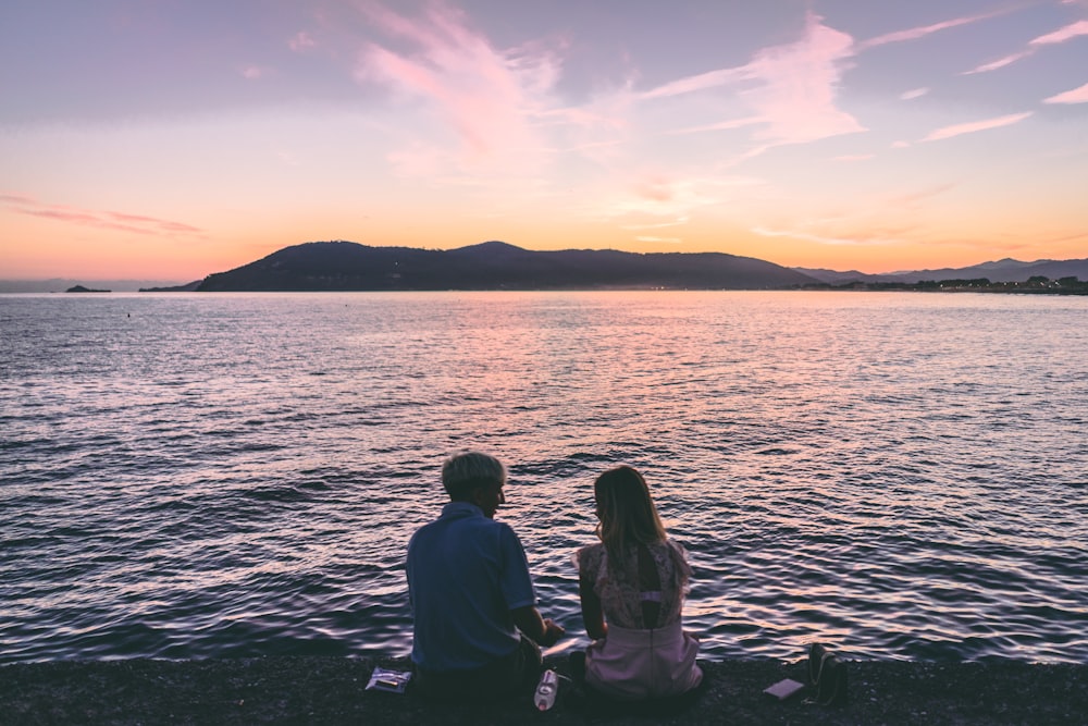 couple sitting on seashore during sunset