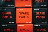 A collection of boxed items stacked neatly, featuring contrasting colors of black and red. The text 'SPARE PARTS' is prominently displayed on each box, accompanied by smaller text and brand name 'BONMAC'.