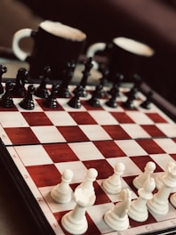 A chessboard set up for a game with black and white pieces in starting positions, accompanied by two mugs, likely filled with coffee or tea, in the background.