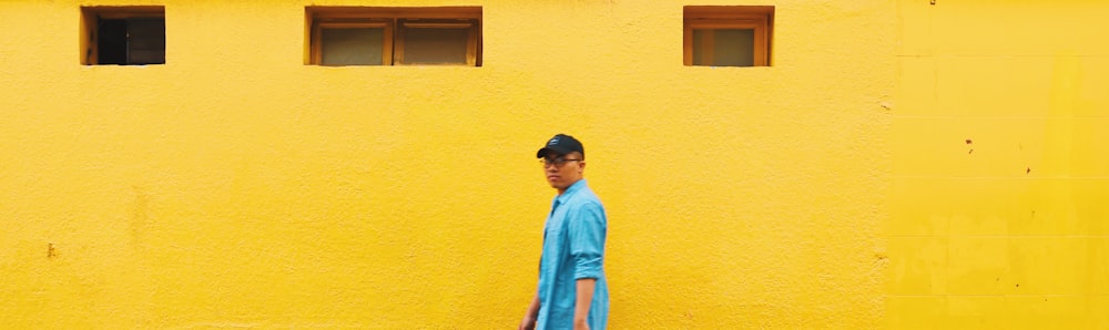man in blue long sleeve shirt standing beside yellow painted wall