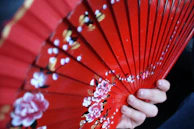 Close-up of a light pink handheld fan being held by a smiling woman on a warm day.