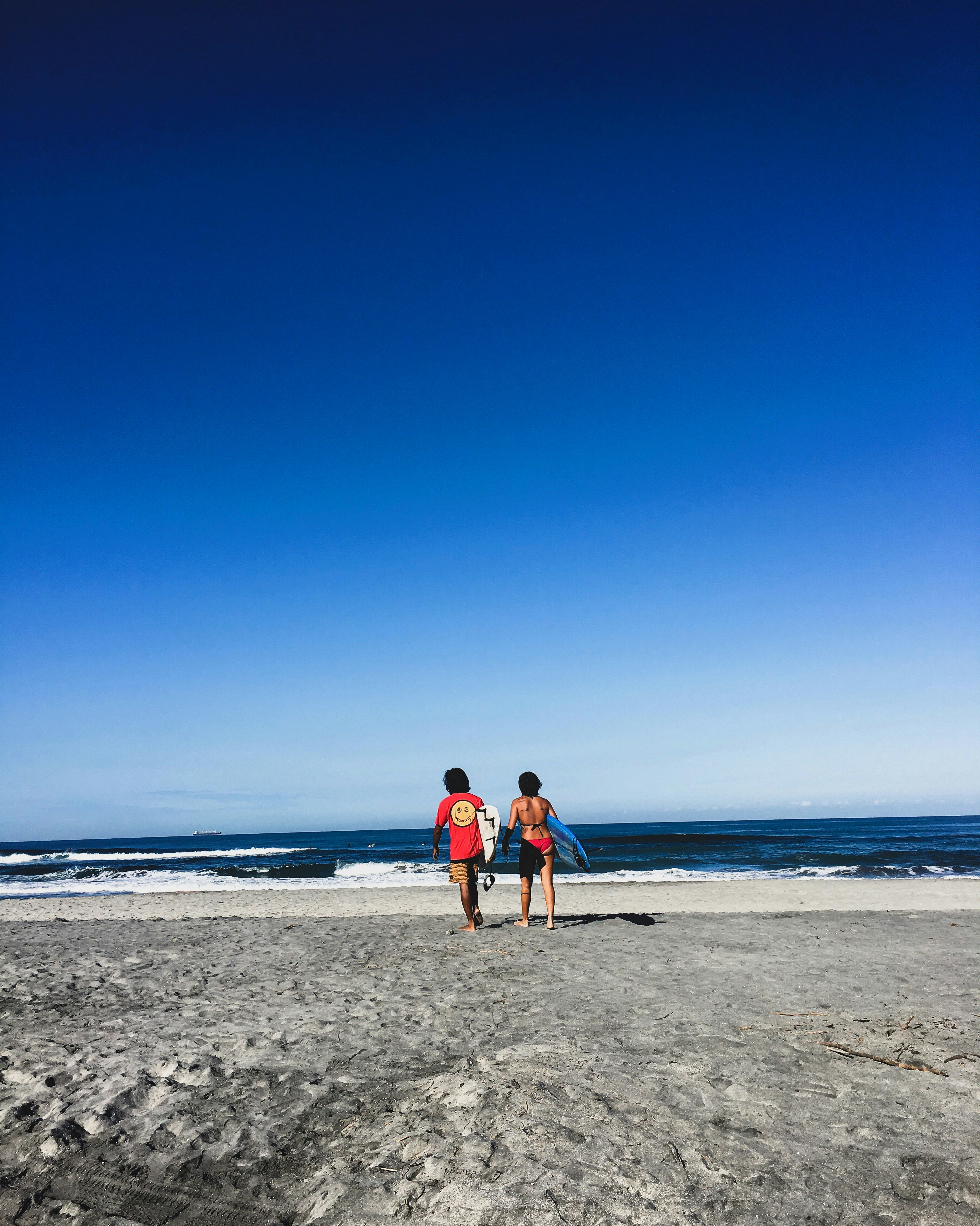 woman in red tank top and blue denim shorts standing on beach during daytime