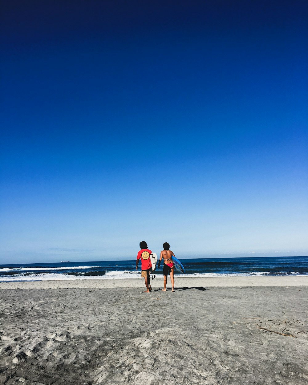 Mujer con camiseta sin mangas roja y pantalones cortos de mezclilla azules de pie en la playa durante el día