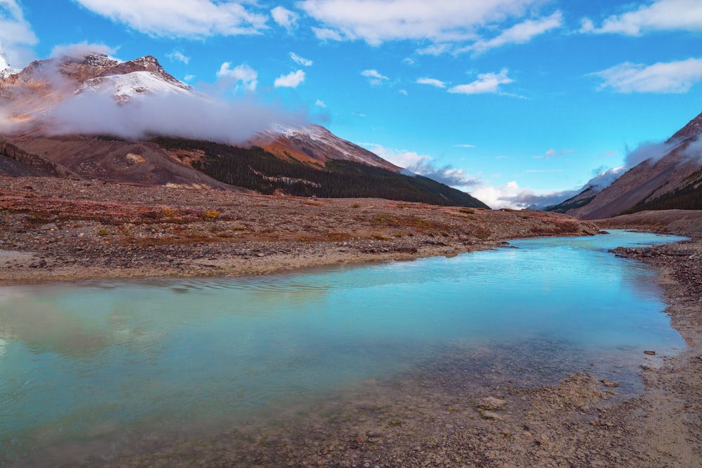 montagne brune et blanche près du plan d’eau sous ciel bleu pendant la journée