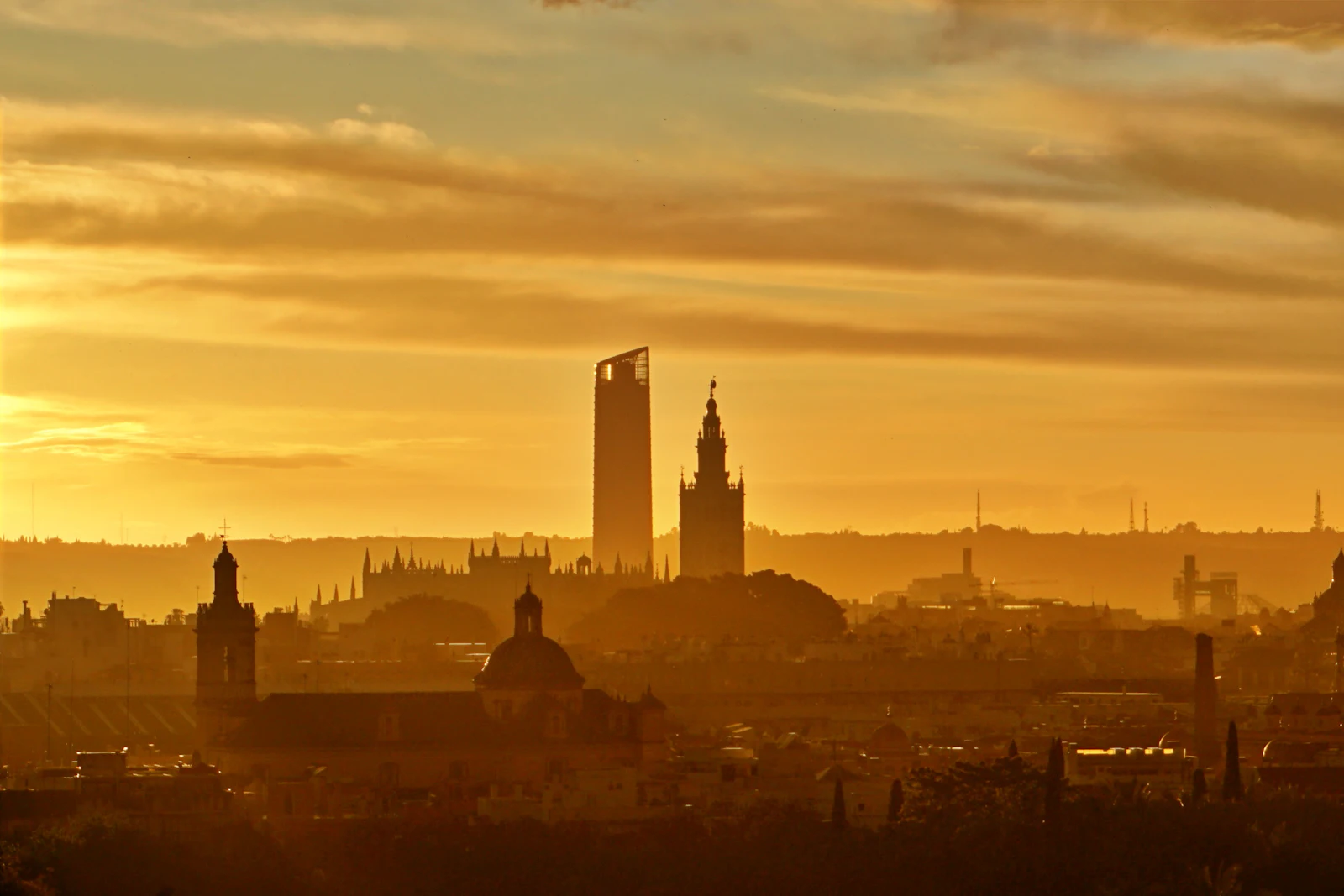 Seville skyline silhouetted against a golden sunset, with church towers rising above the old city