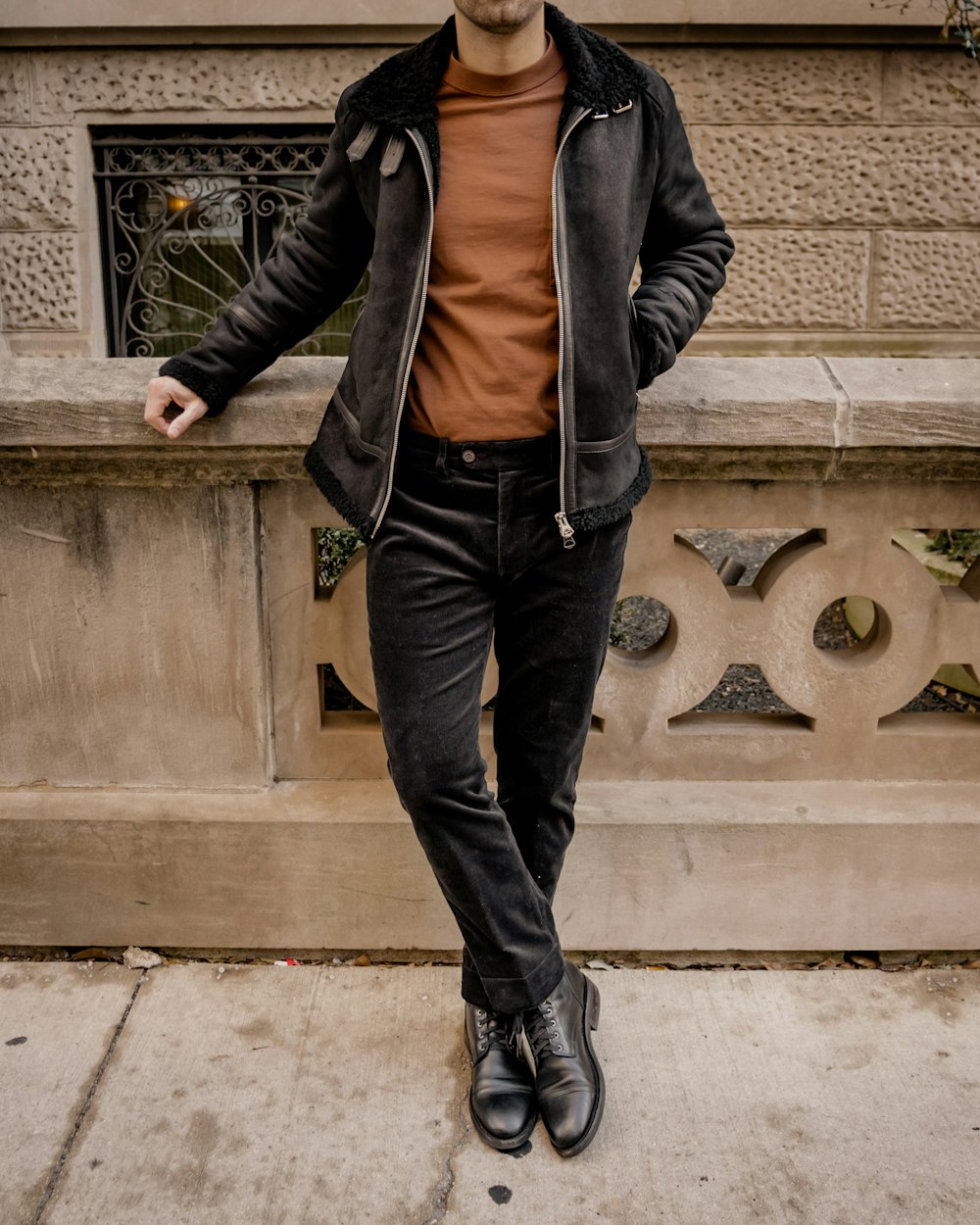 man in black leather jacket and blue denim jeans standing on gray concrete stairs