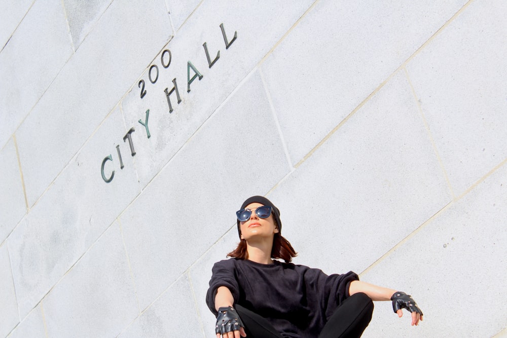 man in black jacket and black pants sitting on white concrete wall during daytime