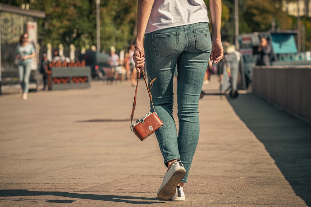 woman in white tank top and blue denim jeans with red sling bag walking on street