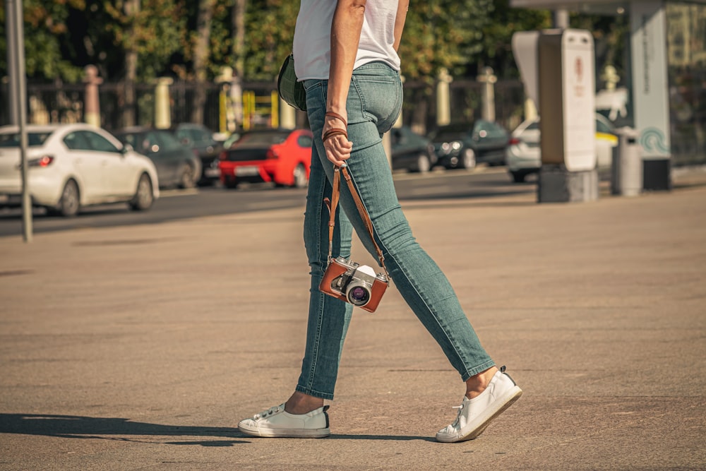 woman in white tank top and blue denim jeans with black and red sling bag walking