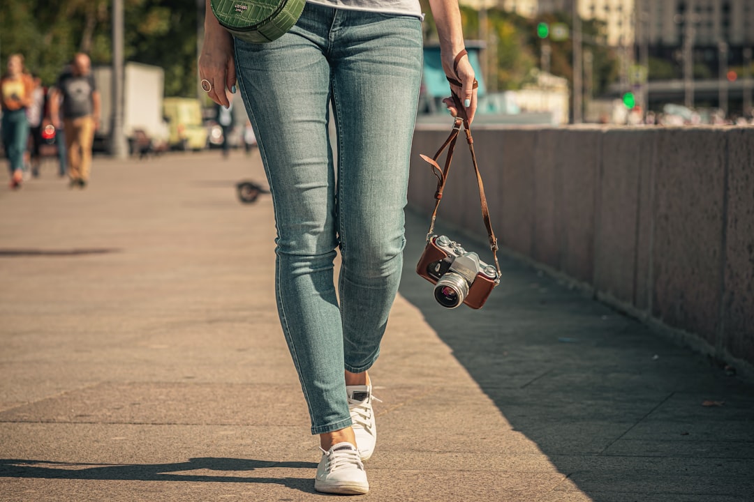 woman in blue denim jeans and white sneakers holding brown leather handbag