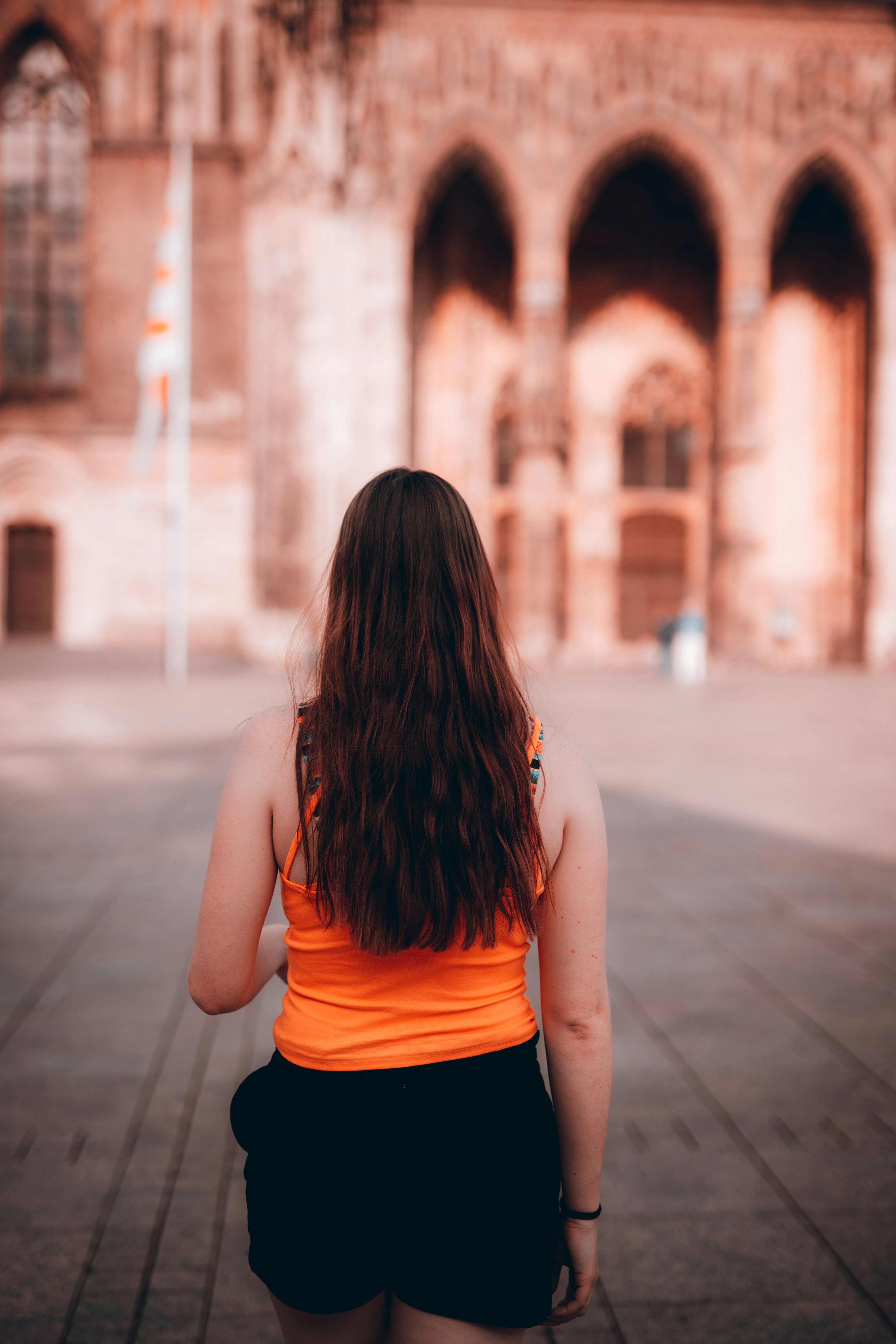 woman in orange tank top standing on sidewalk during daytime