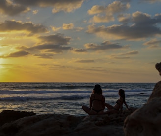 2 women sitting on rock near sea during sunset