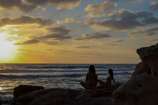 2 women sitting on rock near sea during sunset in Michmoret Israel