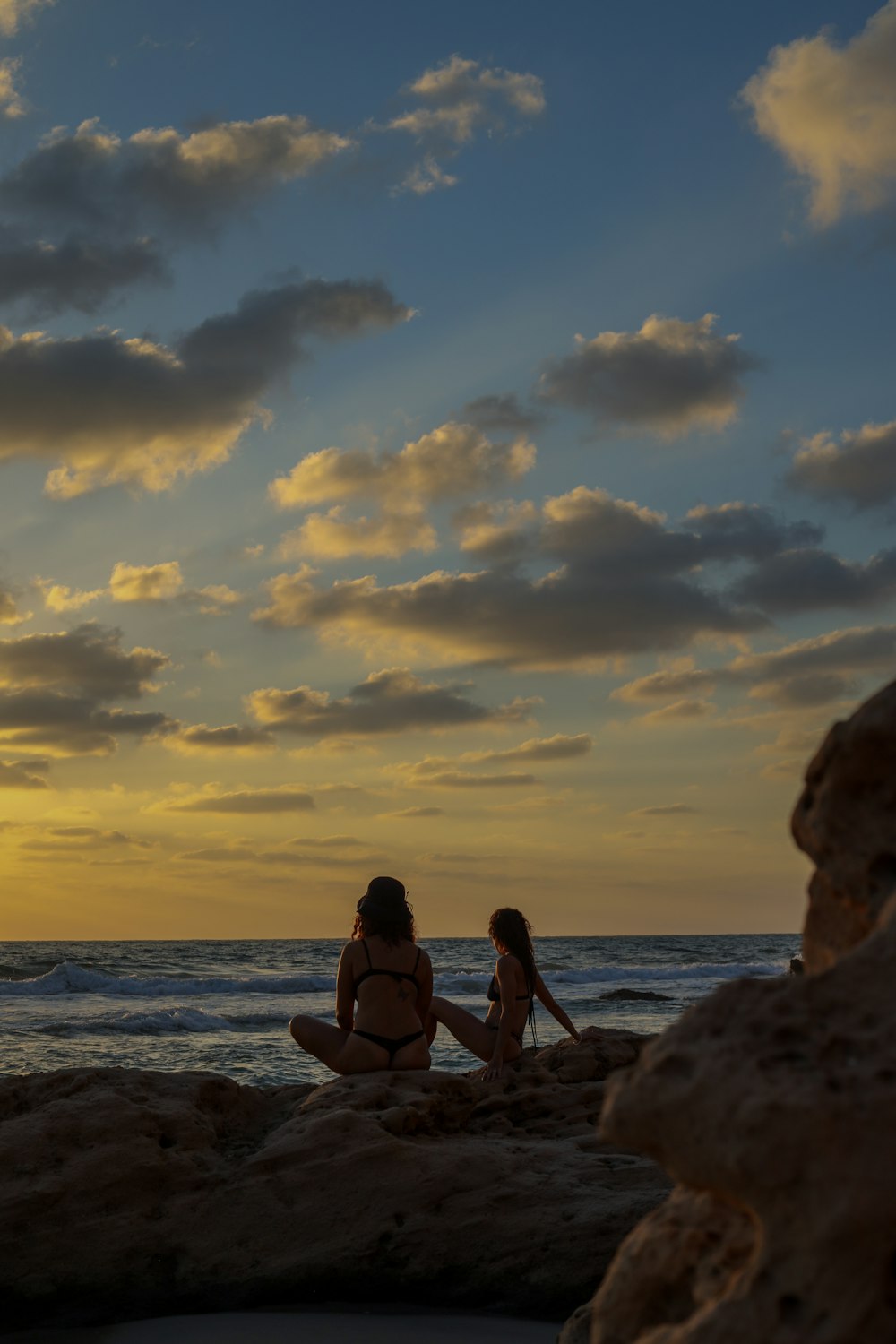 woman in black bikini sitting on rock near sea during sunset