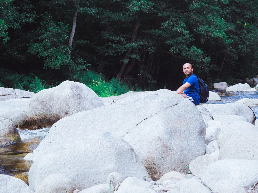 灰色の岩の上に座る青いTシャツの男