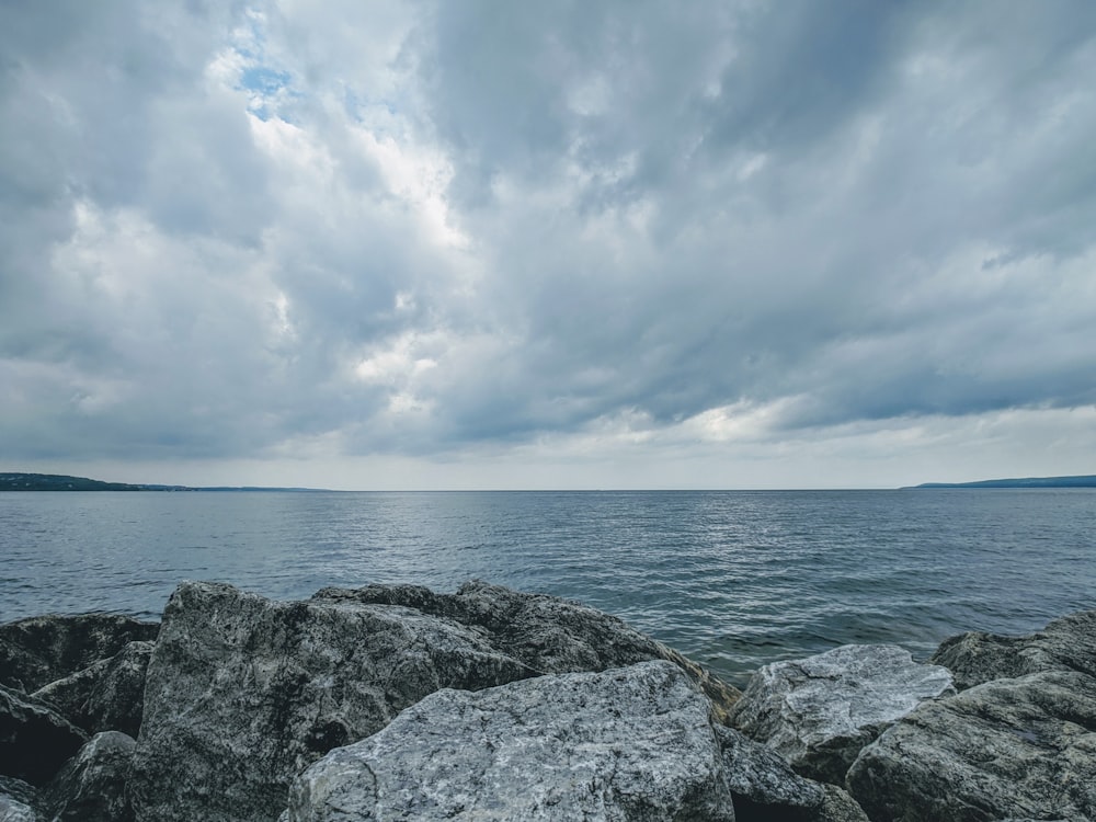 graues felsiges Ufer unter weißen Wolken und blauem Himmel tagsüber