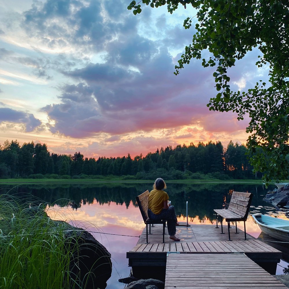 man in black jacket sitting on brown wooden bench near lake during daytime