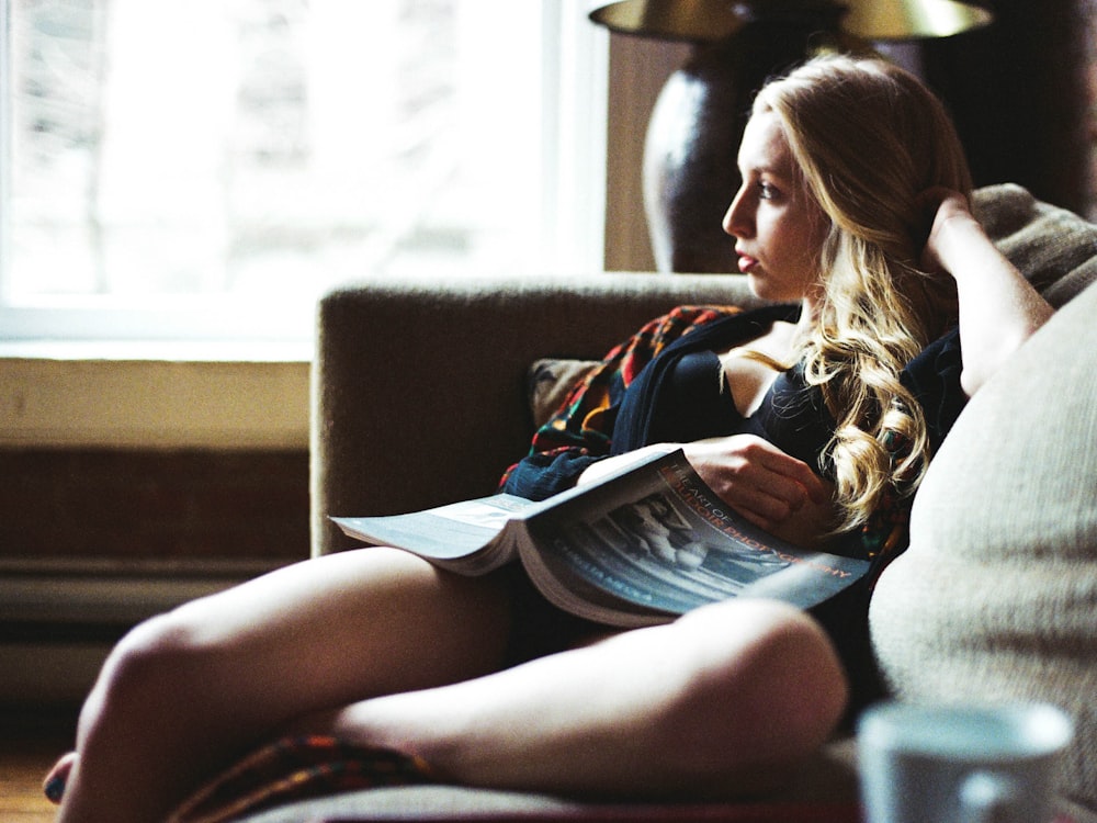 woman reading book sitting on couch