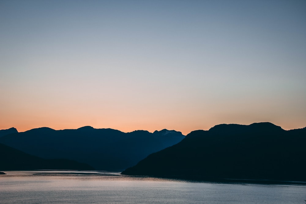 silhouette of mountain near body of water during sunset