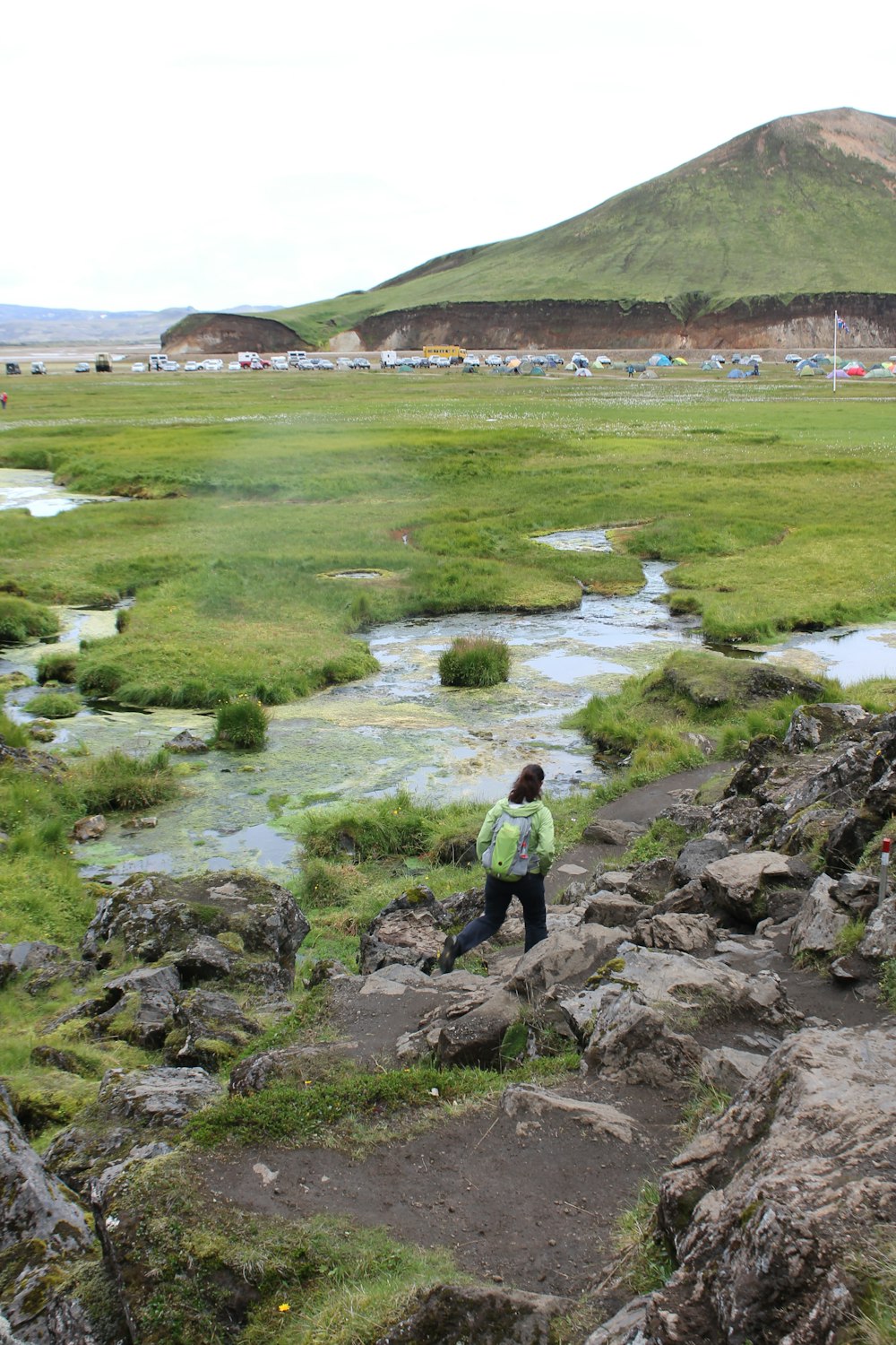 man in green jacket standing on rock near lake during daytime