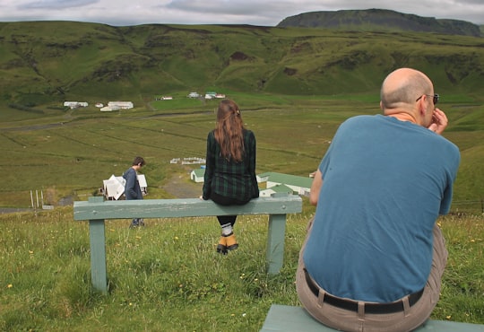 man and woman sitting on white wooden bench on green grass field during daytime in Geysir Iceland