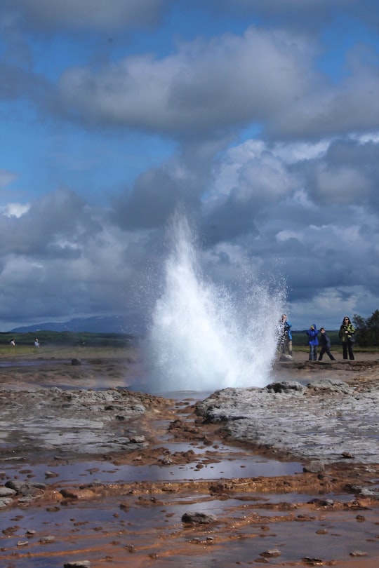 people standing on beach shore under white clouds and blue sky during daytime in Geysir Iceland