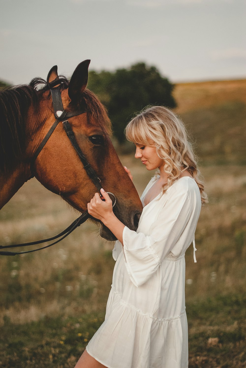 woman in white robe holding brown horse during daytime