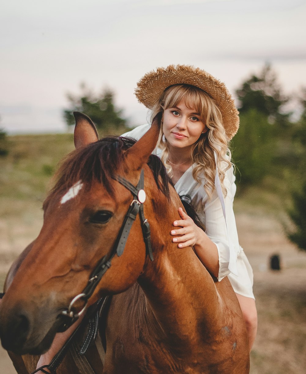 woman in white long sleeve shirt and brown hat standing beside brown horse during daytime
