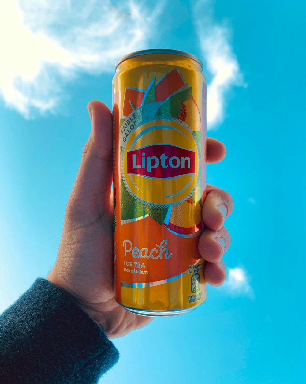 a person holding up a can of lipton peach