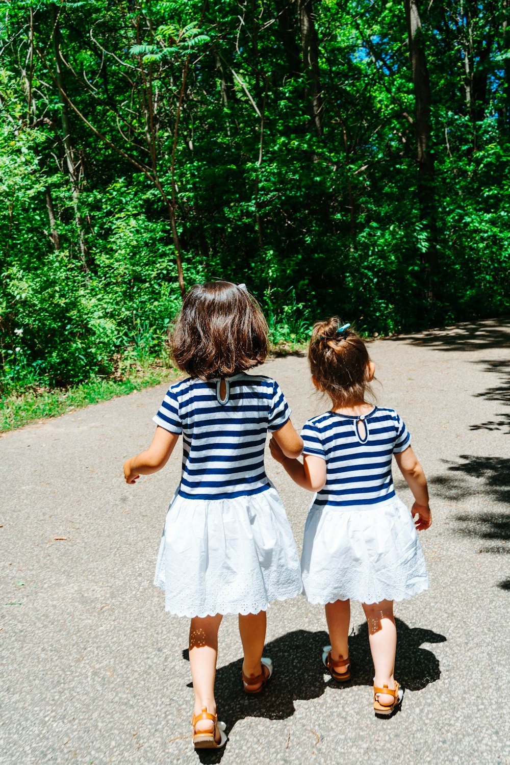 2 meninas no vestido de listras brancas e pretas andando no caminho de concreto cinza durante o dia