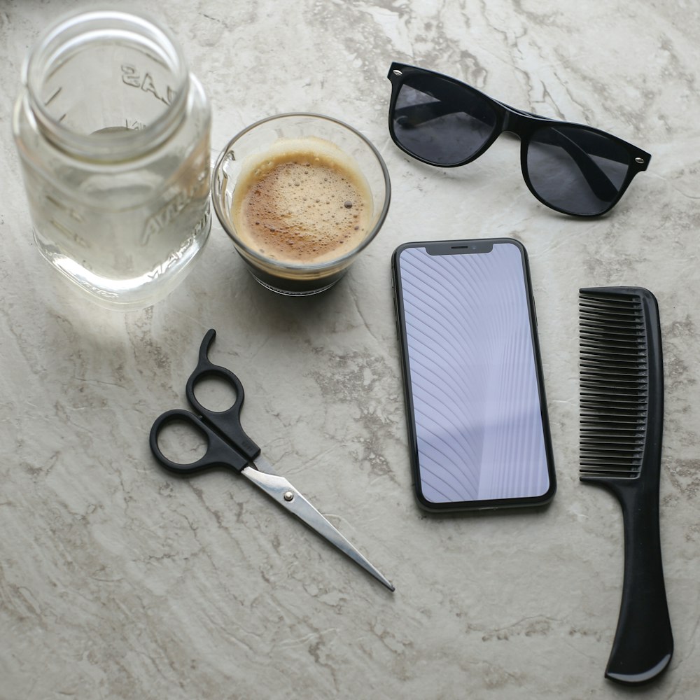 lunettes de soleil à monture noire à côté d’une tasse en verre transparent et de ciseaux à manche noir