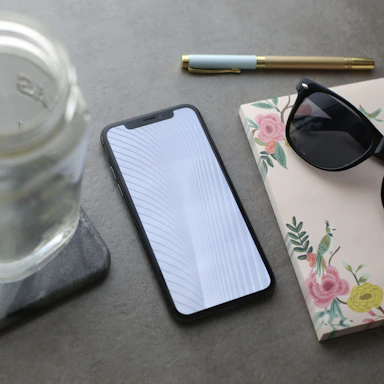 A stylish flat lay of a smartphone, sunglasses, and a chic notebook on a sleek black surface.