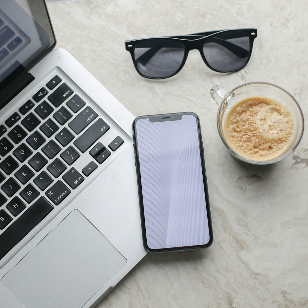 black framed sunglasses beside white ceramic mug and macbook pro