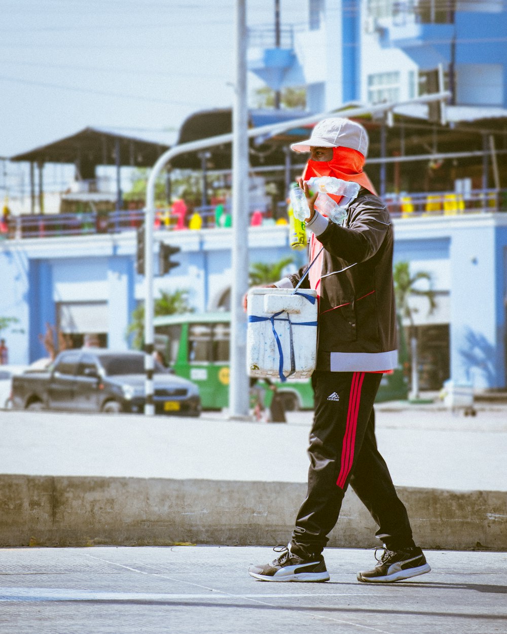 Hombre con camisa roja y pantalones negros con gorra roja de pie en la acera durante el día