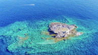 A small island surrounded by turquoise water, seen from a boat.