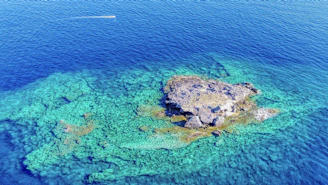 A small island surrounded by turquoise water, seen from a boat.