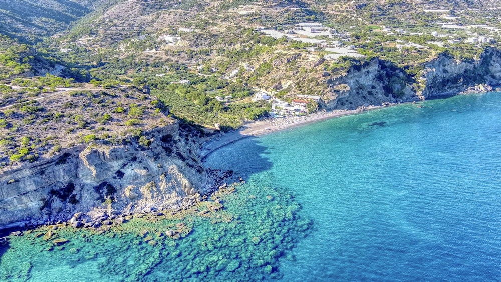 Vue aérienne de la montagne verte et grise au bord de la mer bleue pendant la journée