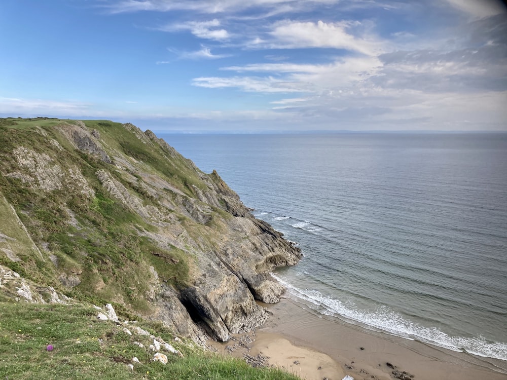 green and brown mountain beside sea under blue sky during daytime