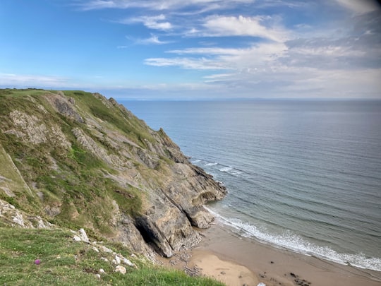 green and brown mountain beside sea under blue sky during daytime in Three Cliffs Bay United Kingdom