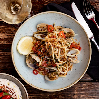 A vibrant plate of fresh seafood pasta garnished with herbs and lemon wedges.