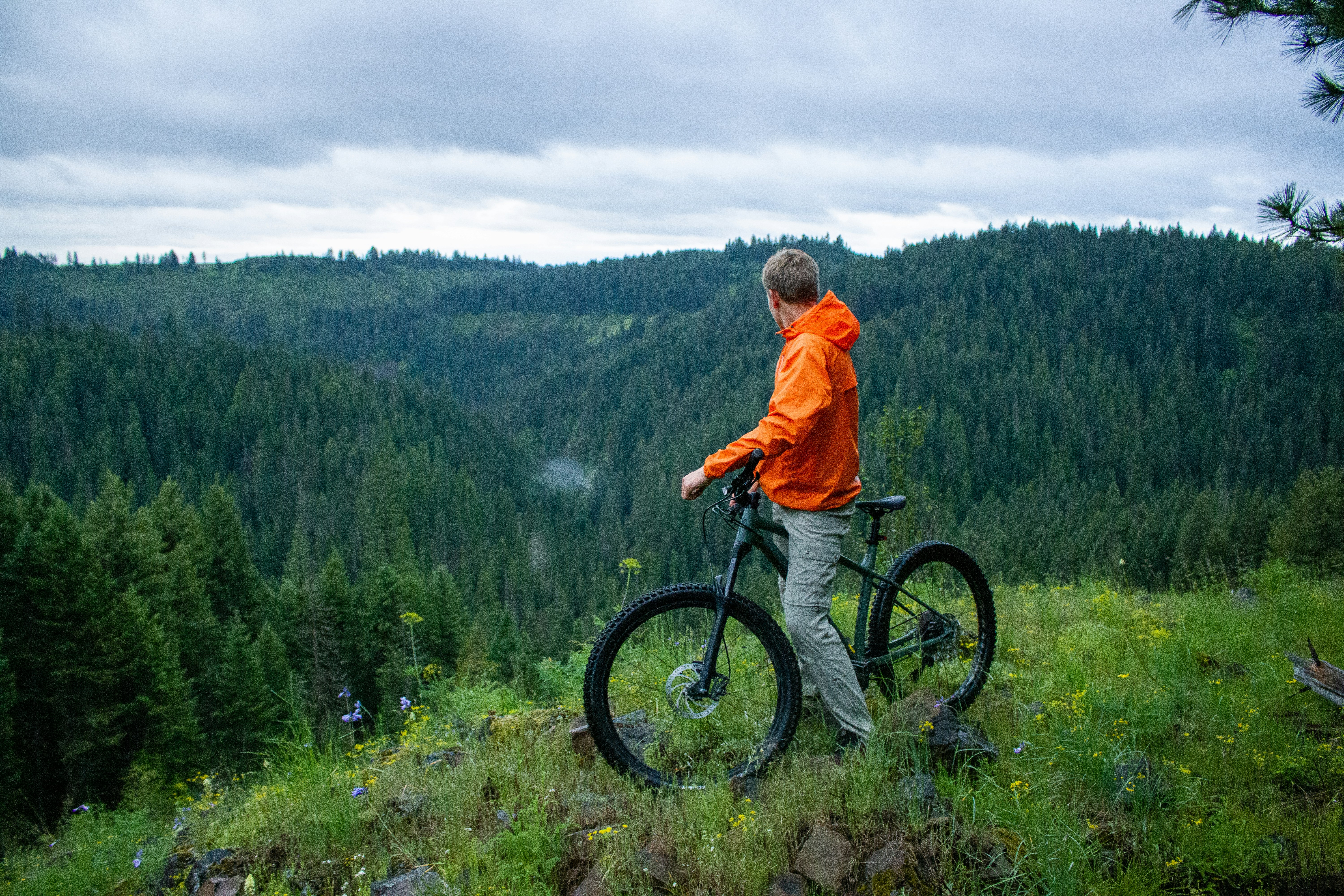 man in orange hoodie riding black mountain bike on green grass field during daytime