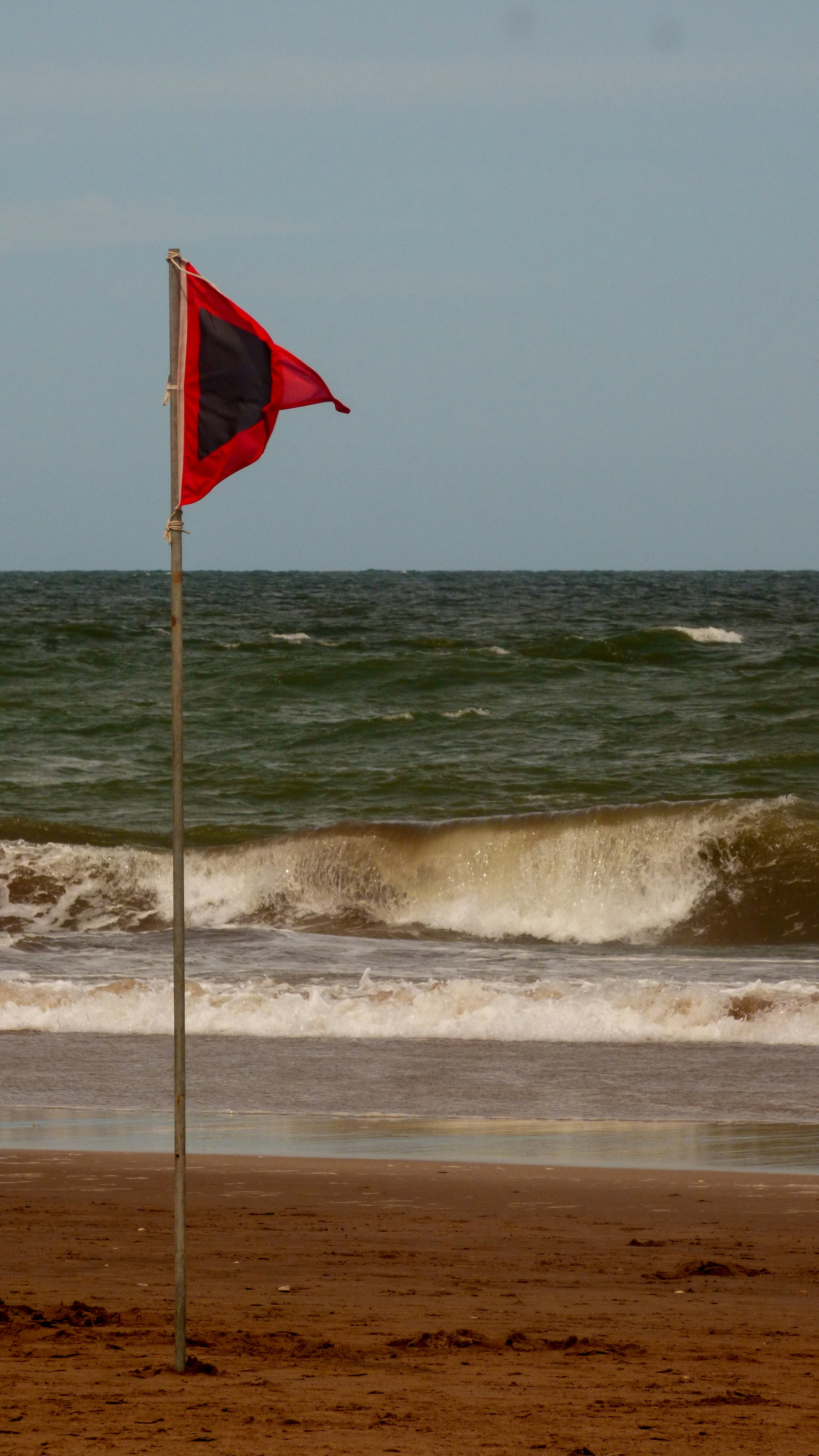 red flag on pole by the sea during daytime