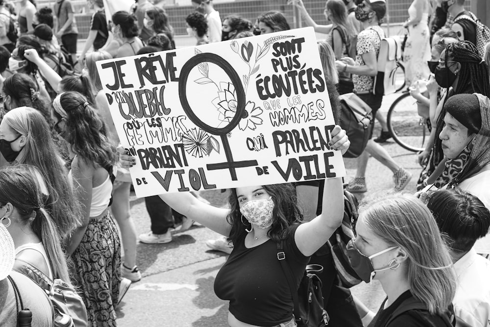 grayscale photo of woman holding white and blue signage